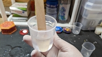 a plastic mixing cup with clear resin and a wooden mixing stick.